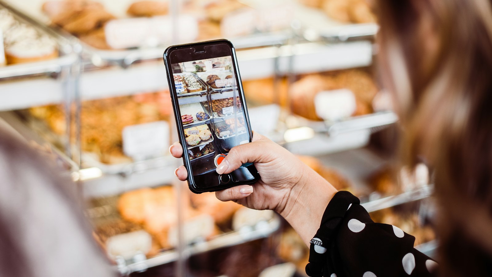 Mujer haciendo una foto con el móvil al escaparate de una pastelería